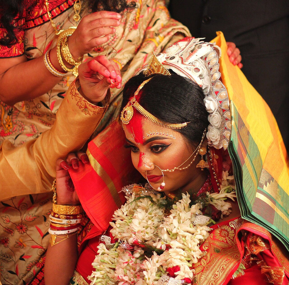 Bengali Hindu bride during sindoor daan, with vermilion on her forehead, gold headpiece and nath, and tuberose garlands