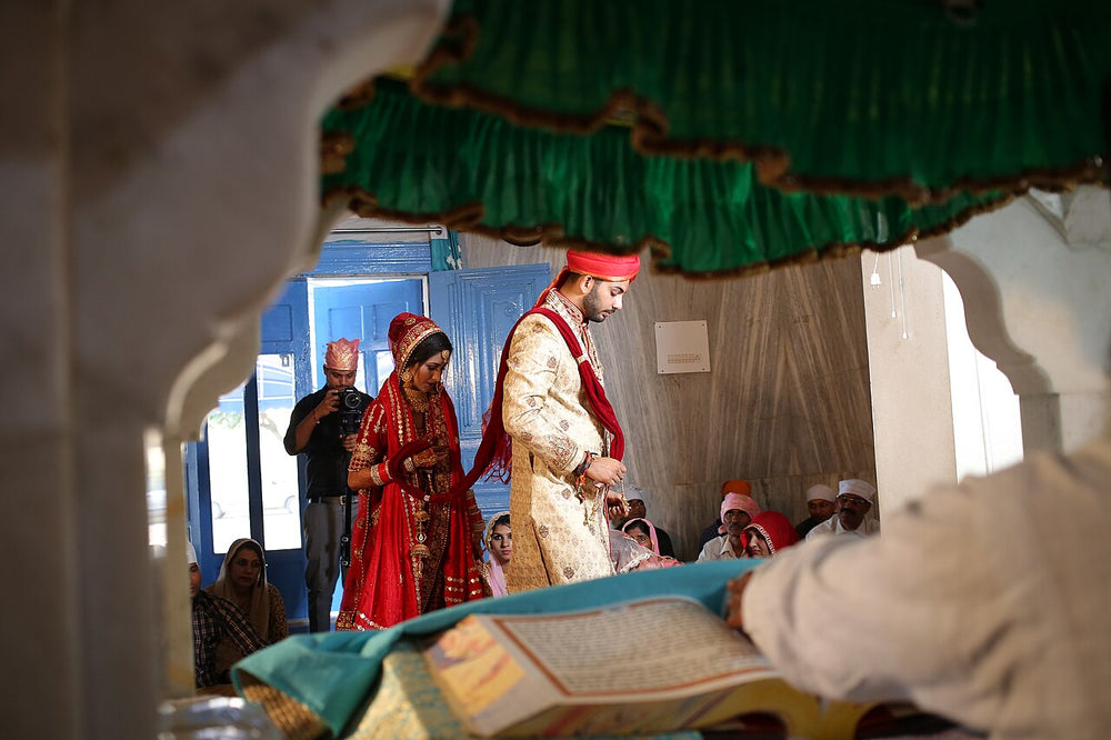 Bride in red lehenga and groom in cream sherwani and red turban at an Anand Karaj in a gurdwara, South Asian wedding