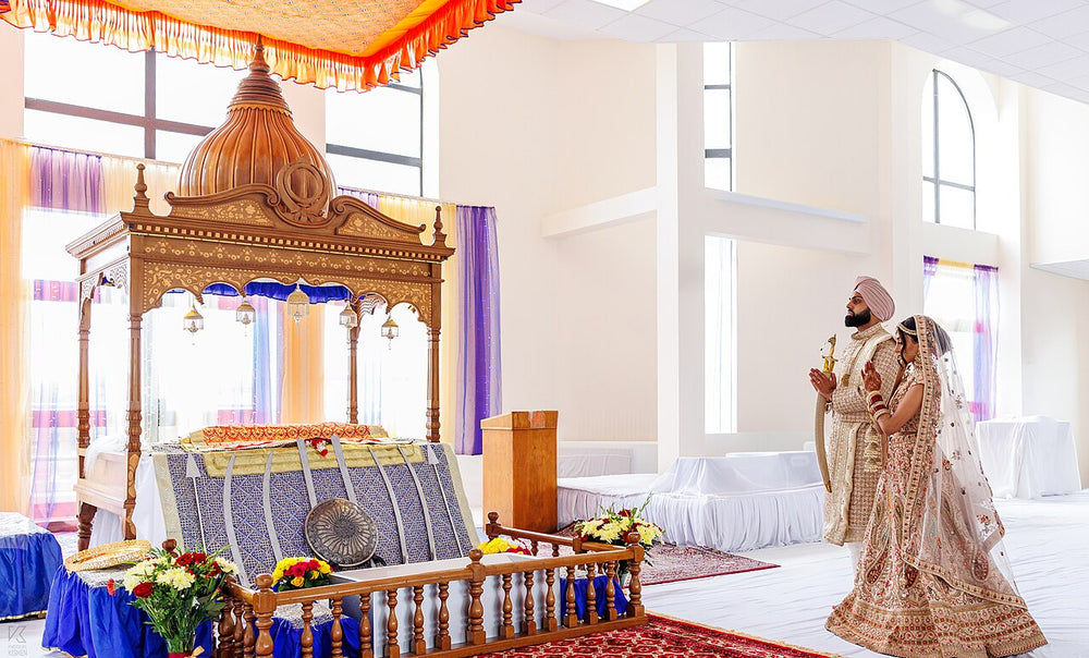 Sikh bride in a embroidered lehenga and groom in a sherwani and turban praying before the Guru Granth Sahib at their wedding