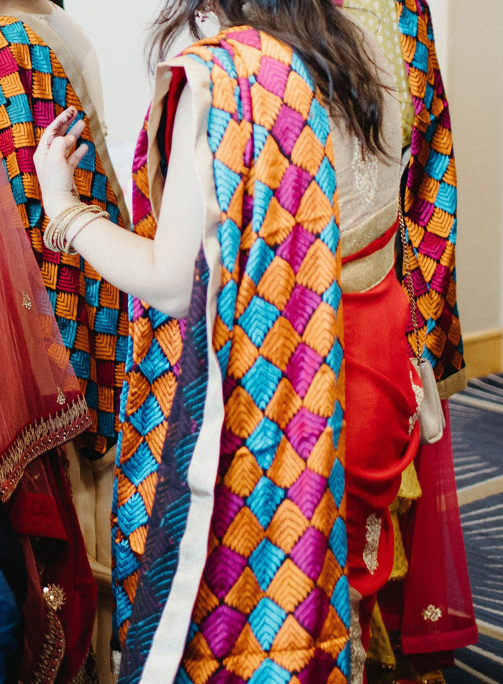 Phulkari stoles in orange, turquoise and magenta worn over red and gold outfits at a Punjabi wedding